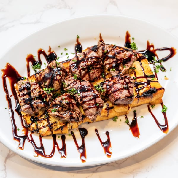 Grilled steak pieces on toasted bread, drizzled with balsamic glaze and sprinkled with parsley.