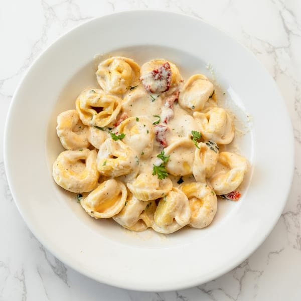DiCicco's tortellini pasta with creamy sauce, sun-dried tomatoes, and fresh parsley in a white bowl.