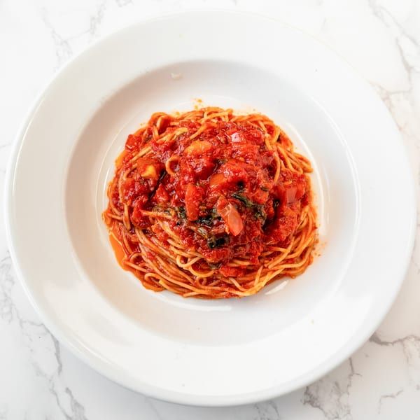 A white bowl filled with spaghetti and a rich red tomato sauce, on a marble surface.