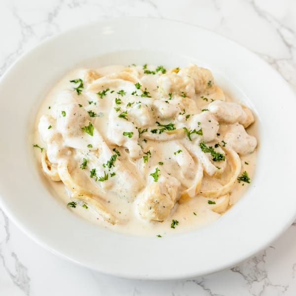 Creamy pasta dish with chicken and parsley in a white bowl on a marble surface.